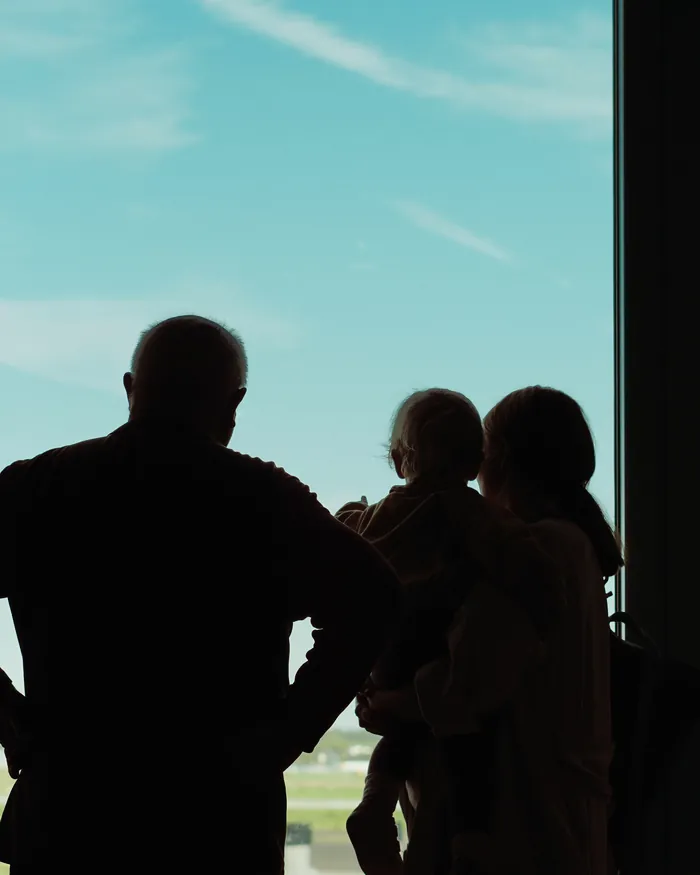 A family at an airport window watching an aircraft