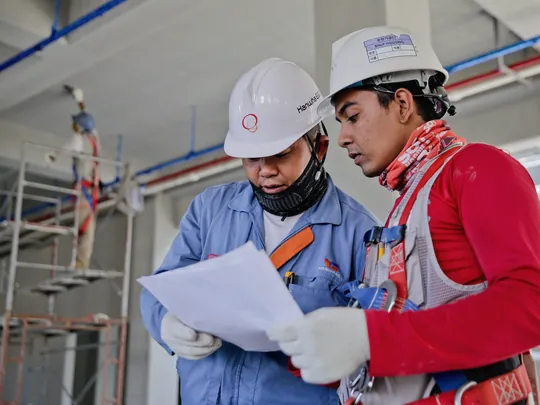 Two engineers in hard hats reading a drawing